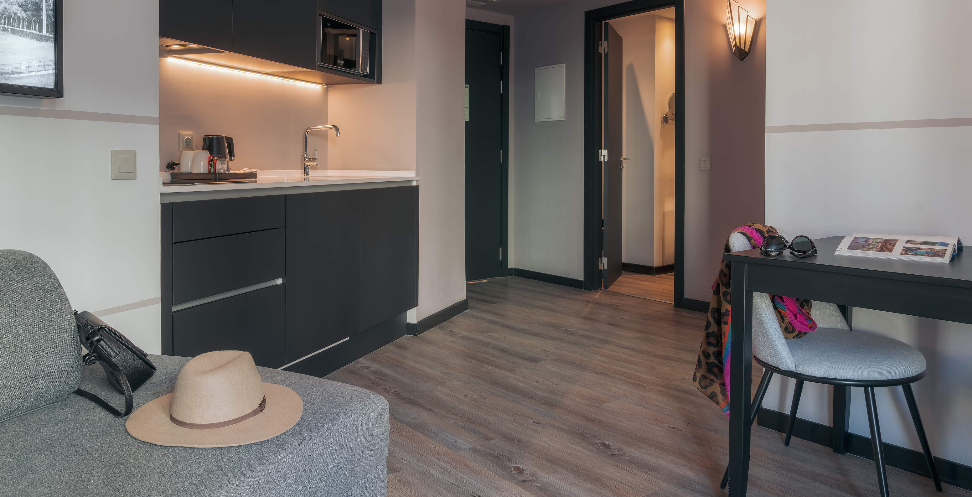 O Double Deluxe Studio do Pestana Lisboa Vintage tem uma kitchenette com micro-ondas, uma mesa com cadeira e um sofá cinzento