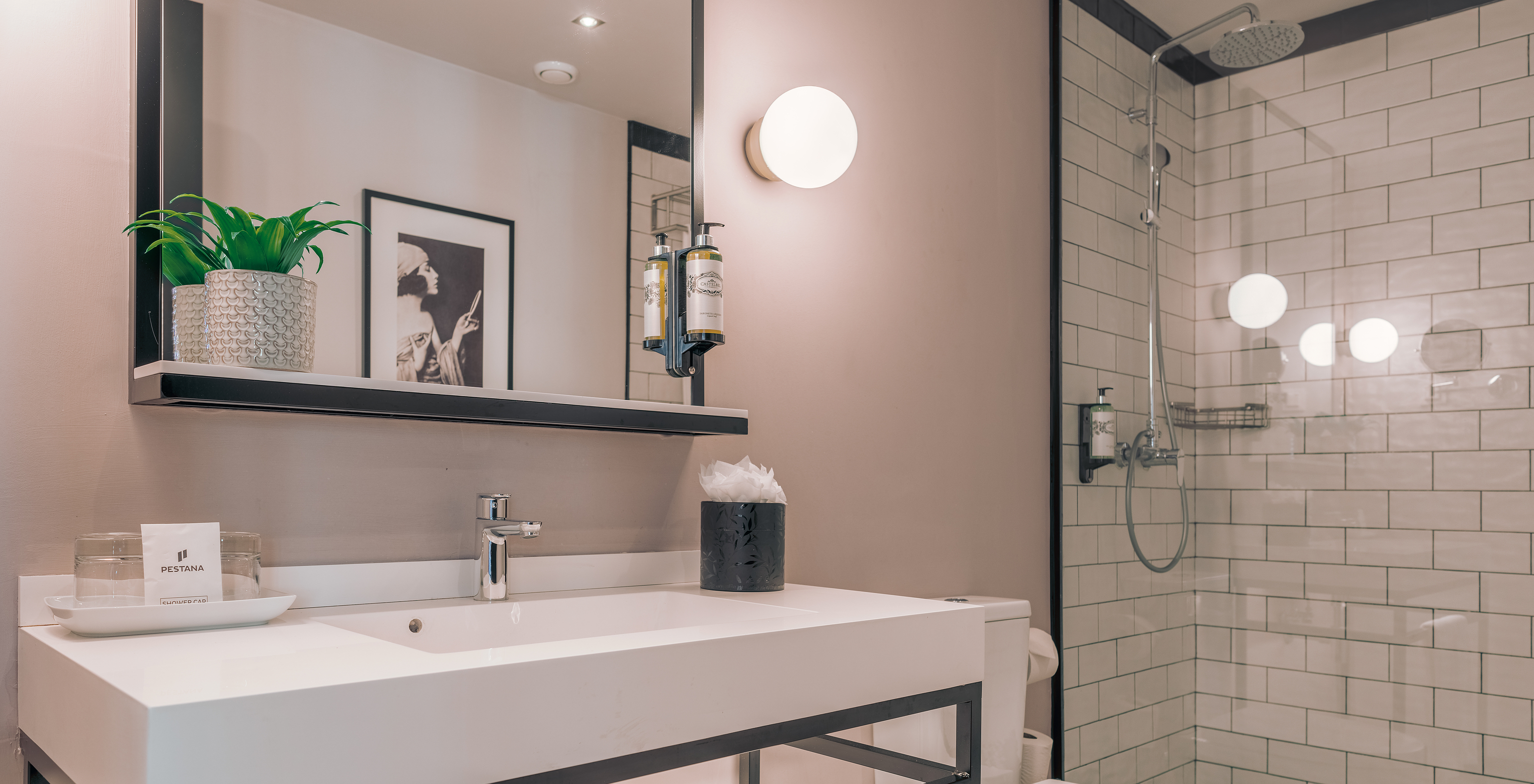 A Junior Suite do Pestana Lisboa Vintage tem uma casa de banho com duche com portas de vidro com detalhes pretos e uma sanita