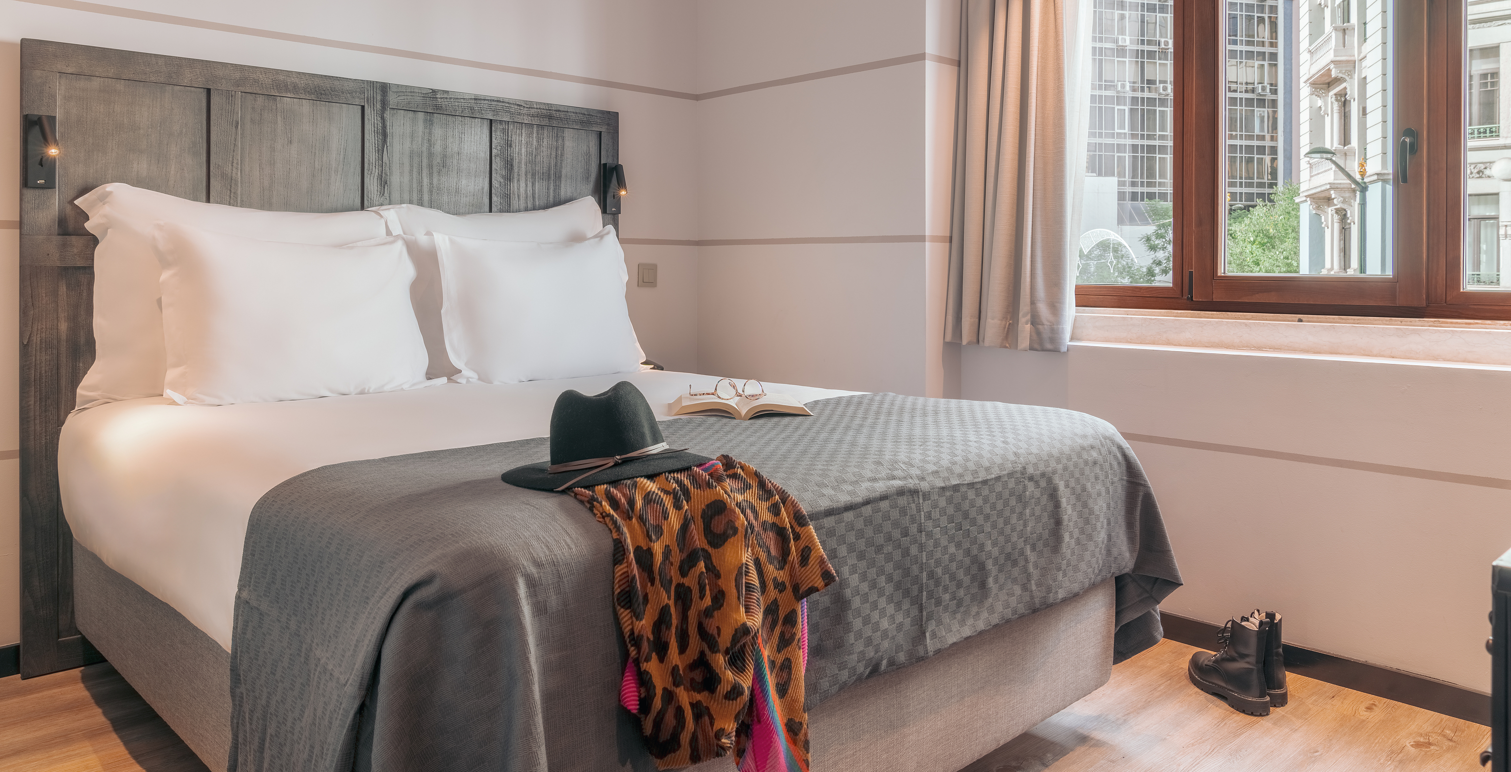 O Vintage do Pestana Lisboa Vintage tem uma cama de casal com cabeceira e uma manta cinzentas, umas botas no chão de madeira