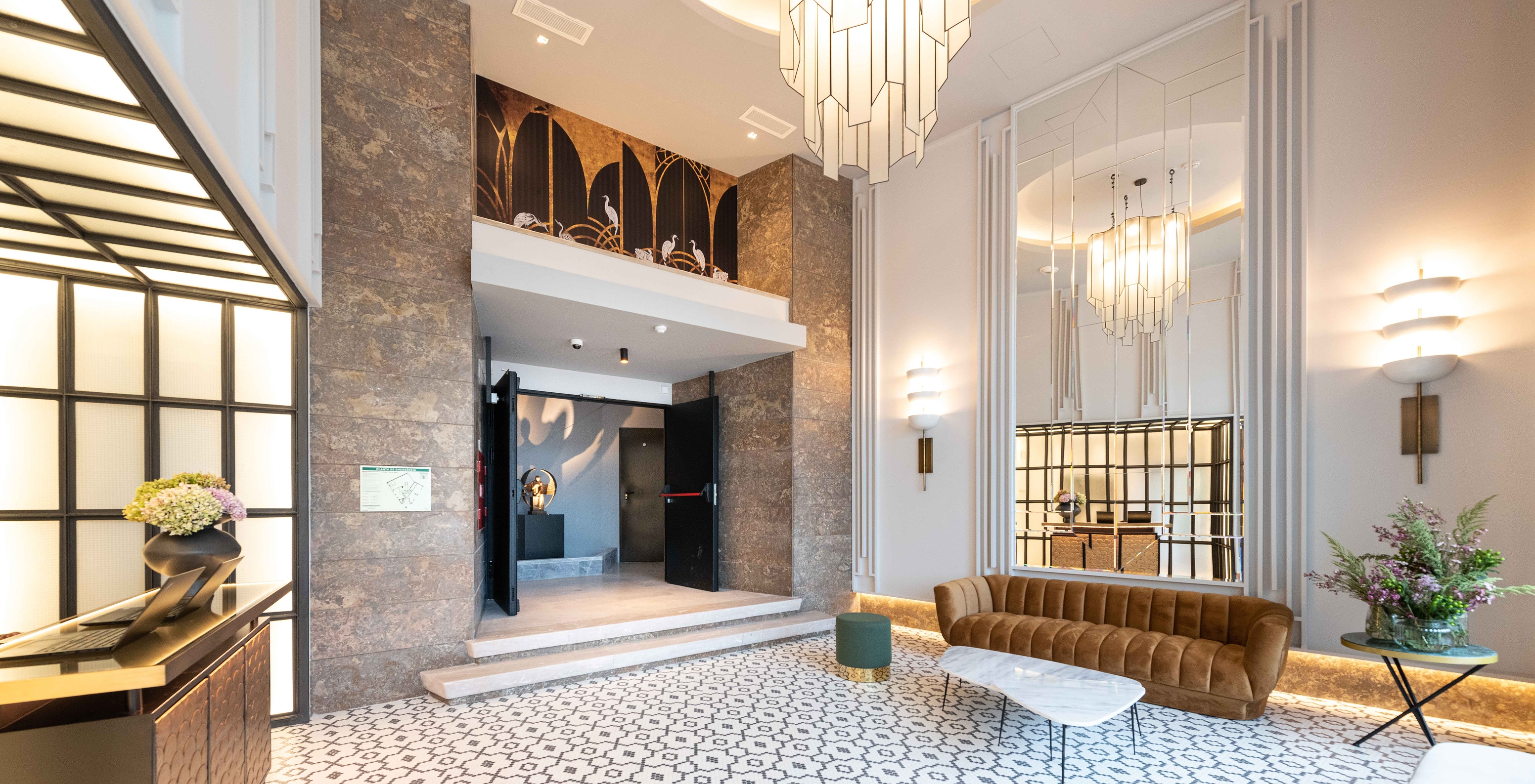 Lounge da receção com espelhos, sofás, mesas de apoio com vasos de flores, um candelabro e um padrão floral no chão
