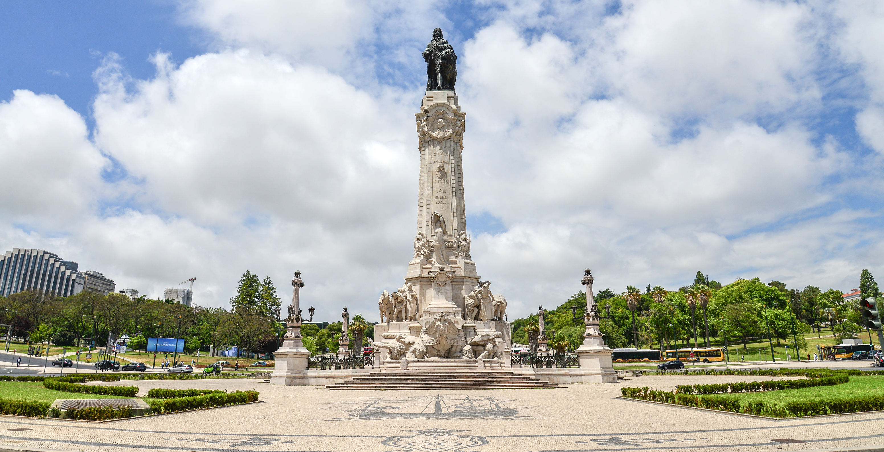Vista de baixo da estátua do Marquês de Pombal, com canteiros e árvores ao redor e o céu nublado