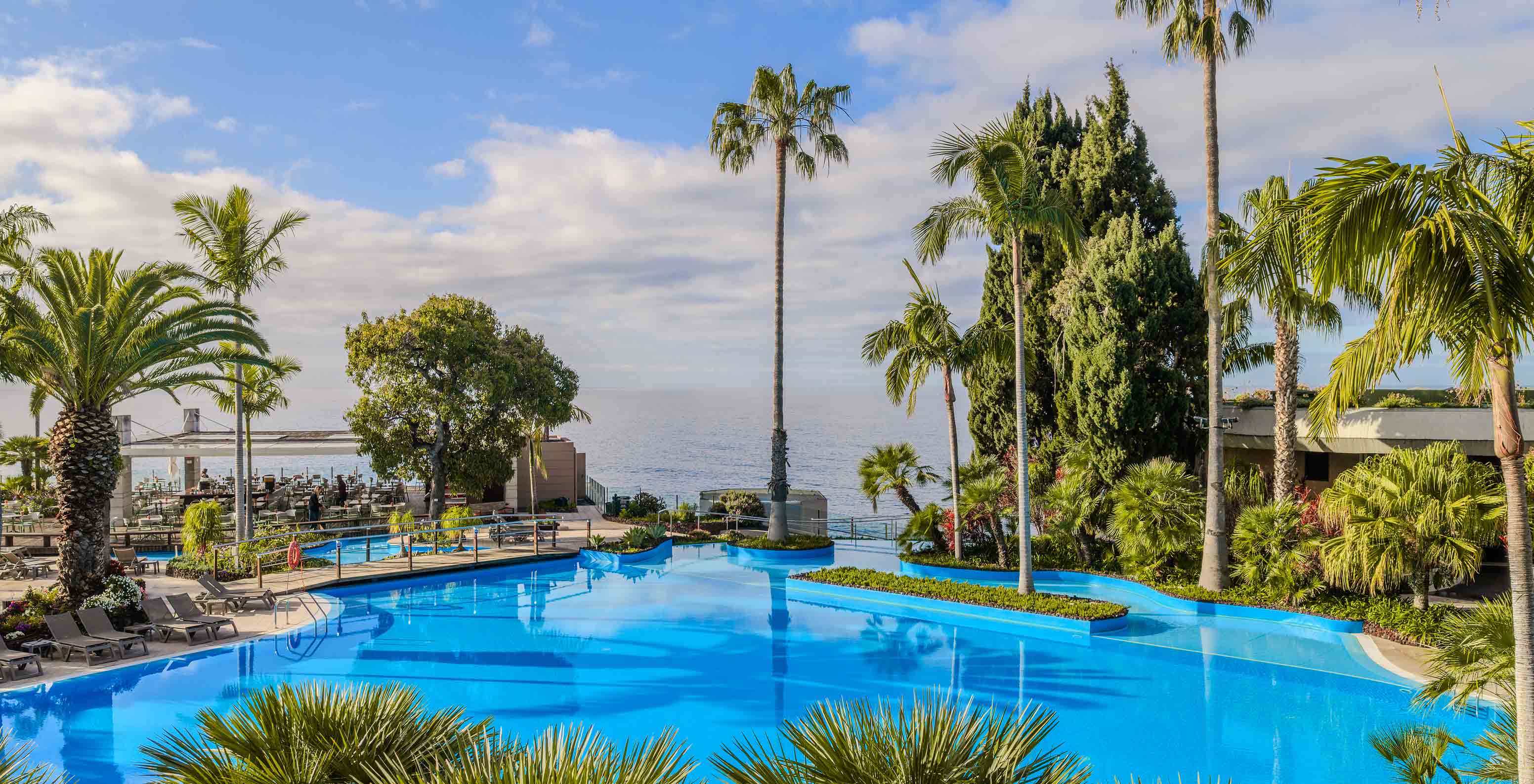 Piscina exterior rodeada por palmeiras junto ao Pestana Carlton Madeira, Hotel 5 Estrelas na Madeira