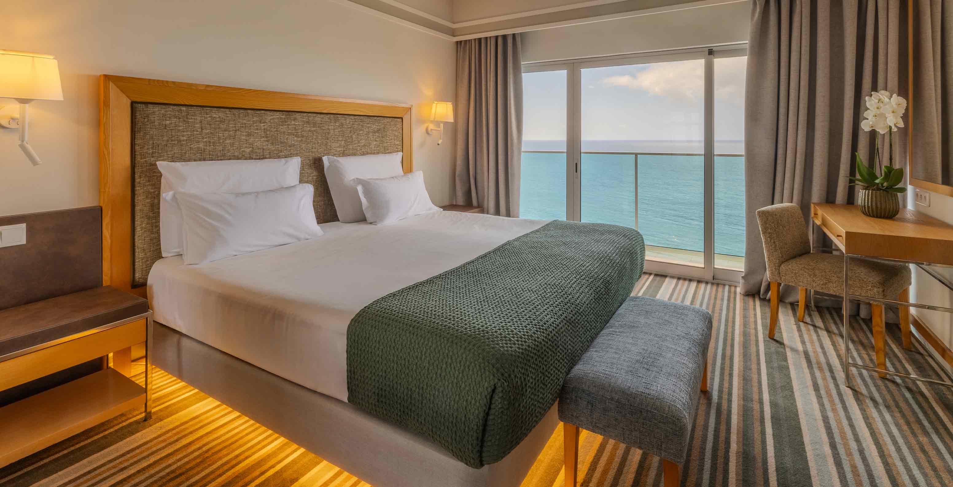 Junior Suite Superior no Pestana Carlton Madeira com cama ampla e varanda voltada para o mar e secretária junto à janela