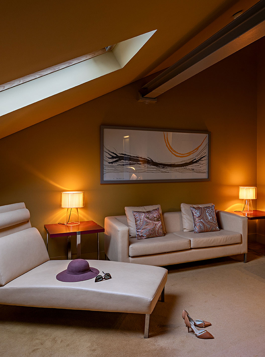 Sala de estar do quarto Loft Attic no Pestana Palácio do Freixo, com sofá bege, poltrona moderna e iluminação suave de abajures