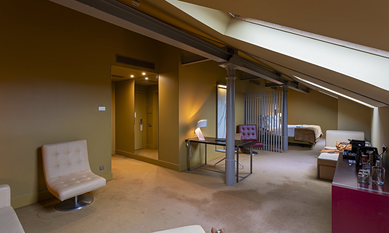 O Loft Ático do Pestana Palácio do Freixo tem um sofá beje em pele, uma secretária e um móvel vermelho 