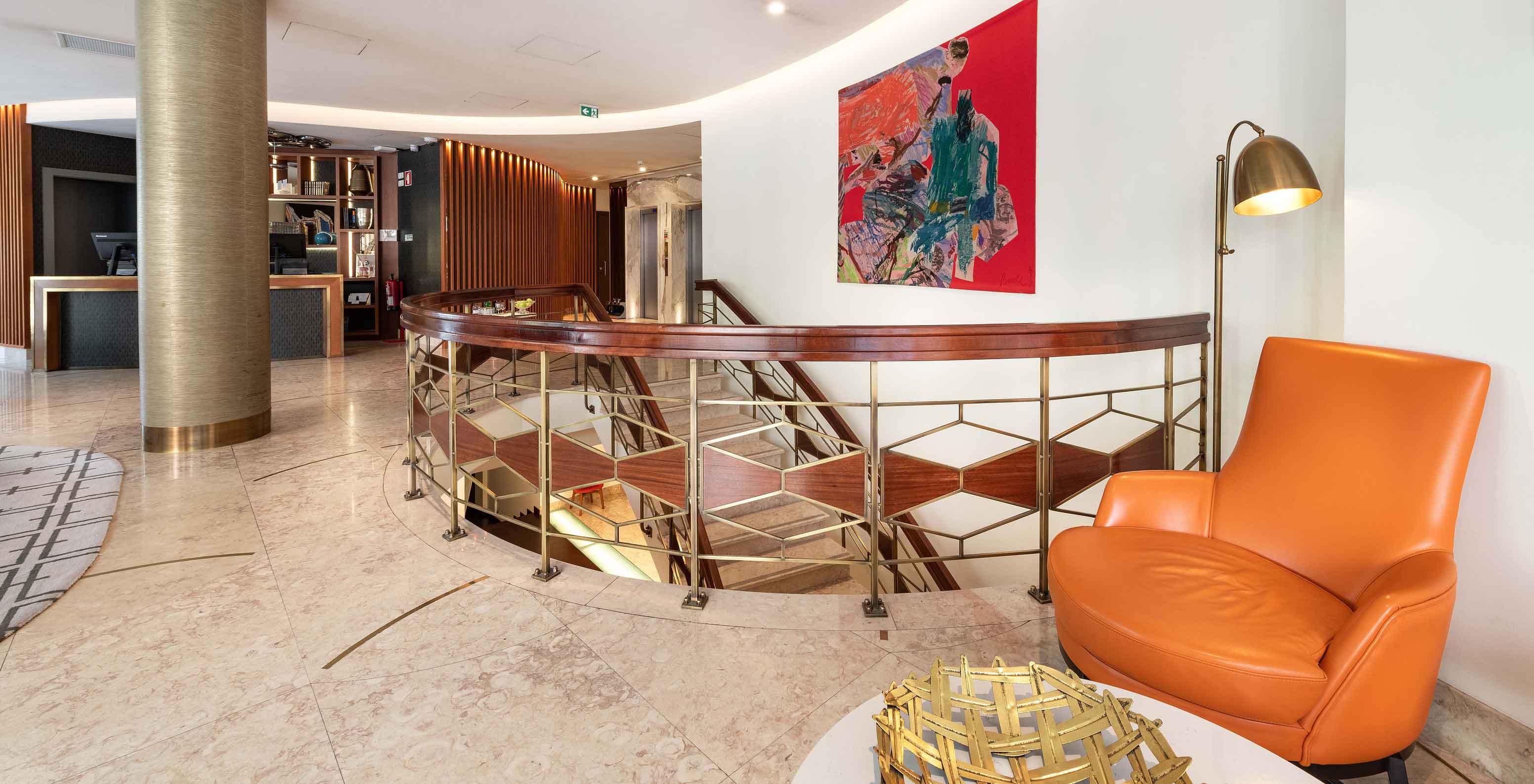 Área interior do Pestana Porto A Brasileira, Hotel 5 Estrelas no Centro do Porto, com poltrona laranja e escadaria elegante
