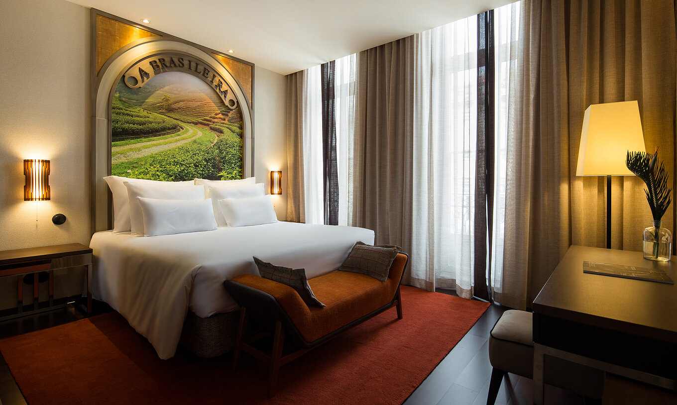 O Deluxe Superior do Pestana Porto - A Brasileira tem uma cama com um mural temático na cabeceira e um banco ao fundo