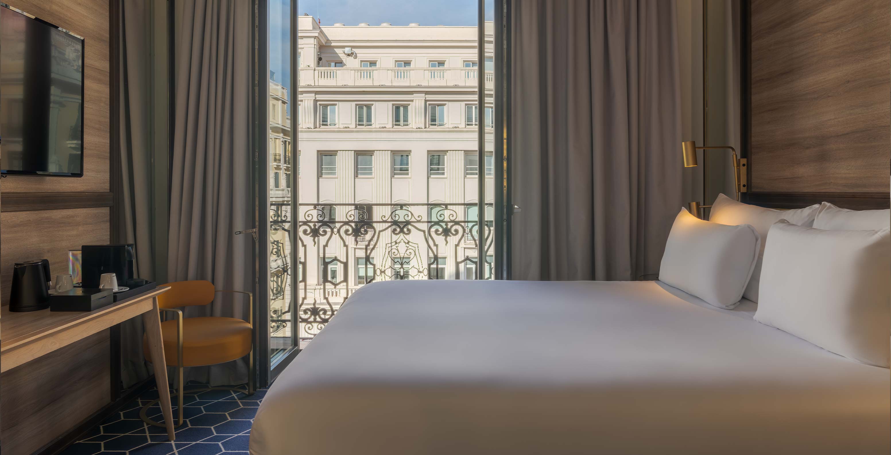 Quarto Deluxe Window no Pestana CR7 Gran Vía Madrid, com cama ampla e varanda voltada para edifícios urbanos