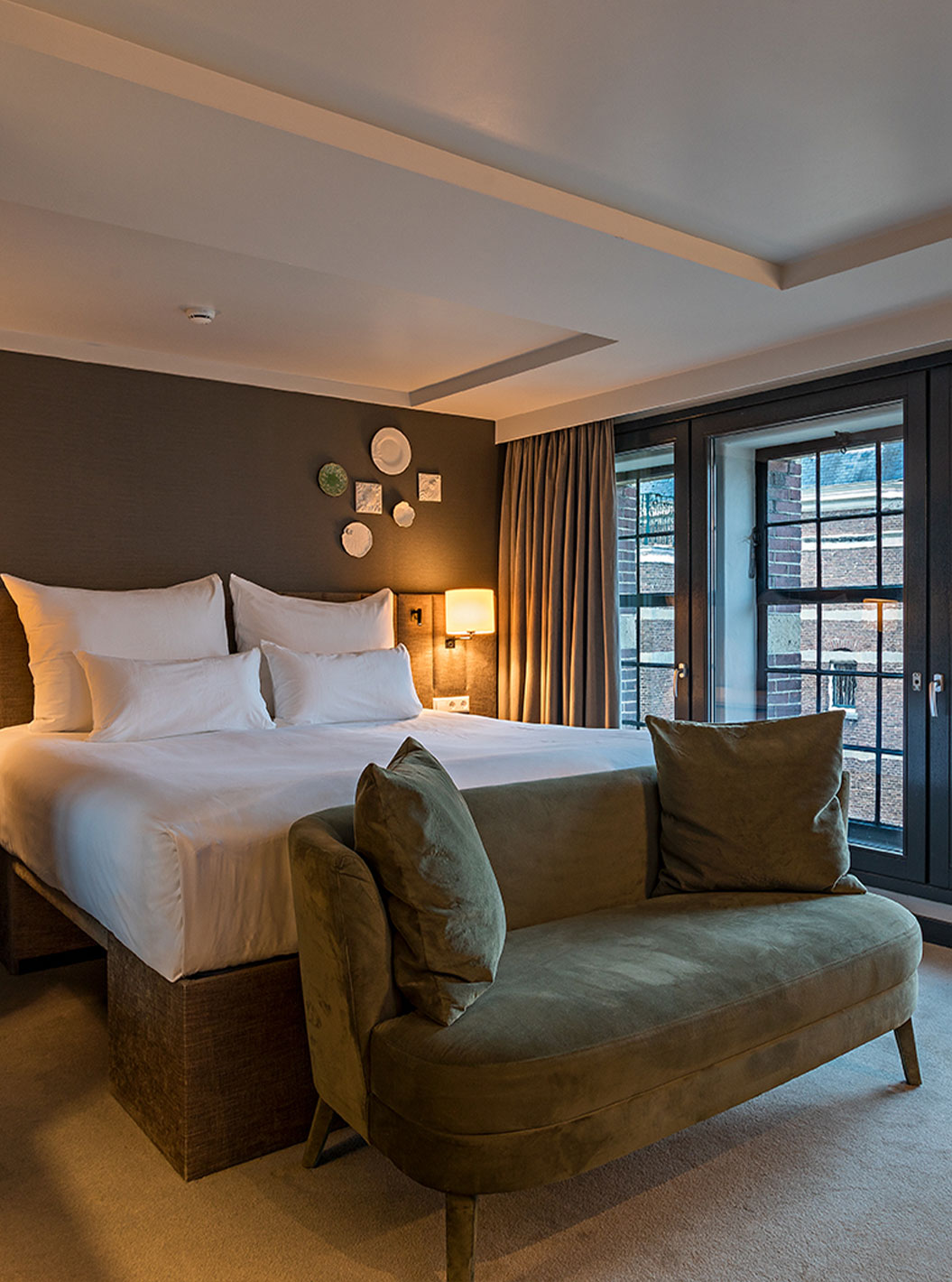 Quarto Deluxe com vista no Pestana Amsterdam Riverside, cama de casal, sofá verde e janelas amplas