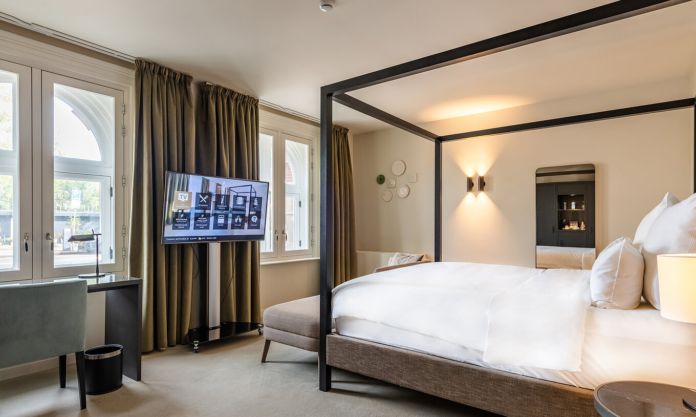 O quarto Premium Deluxe do Pestana Amsterdam Riverside tem uma televisão à frente da cama e uma secretária com cadeira