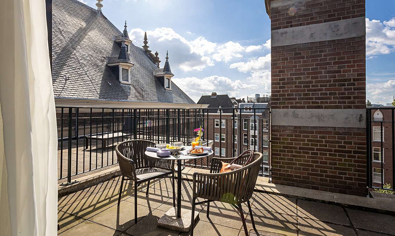 Varanda do quarto Superior Terrace do Pestana Amsterdam Riverside com mesa posta e vista para telhados históricos