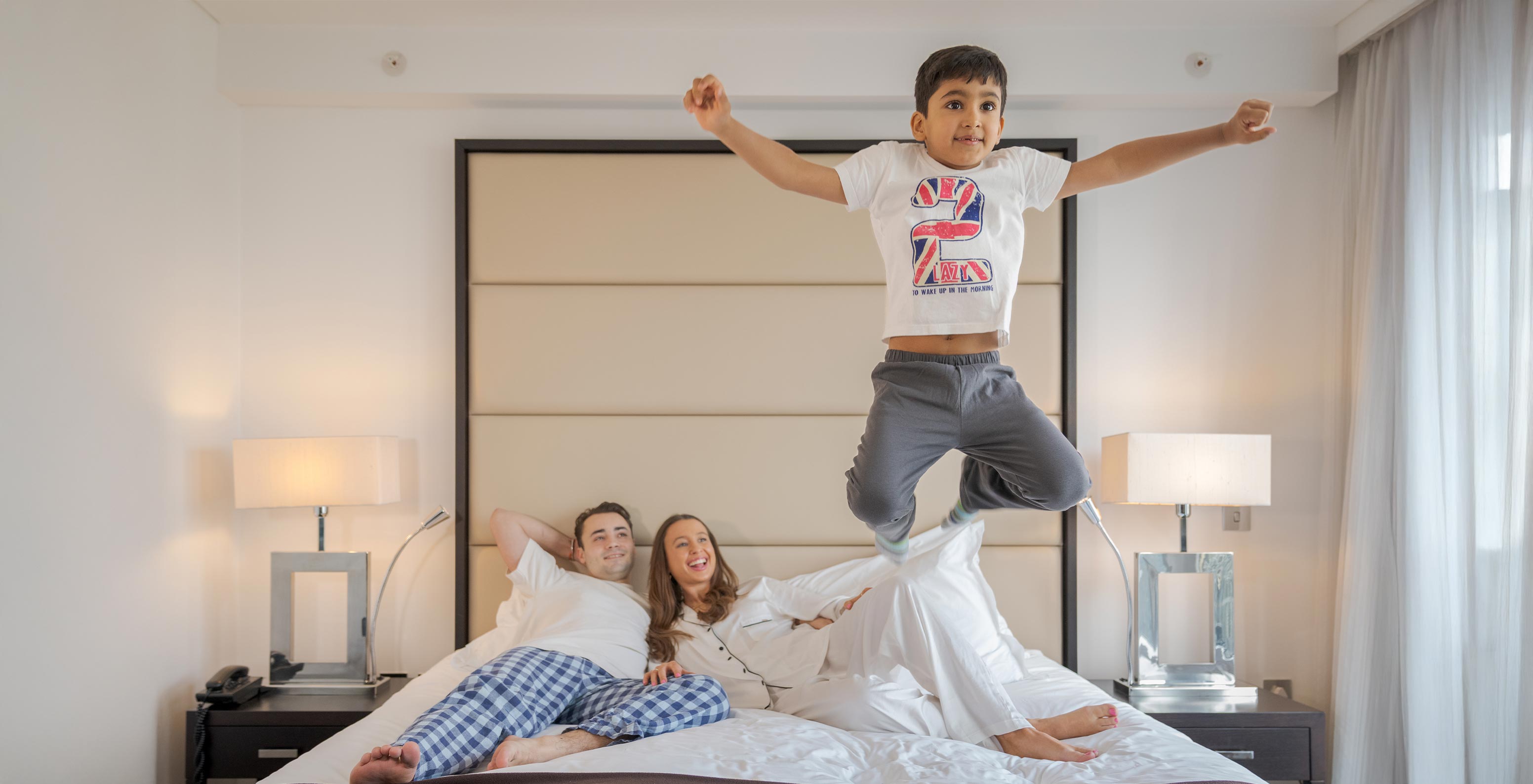 O Deluxe Family do Pestana Chelsea Bridge tem cama de casal com uma família deitada e uma criança a saltar