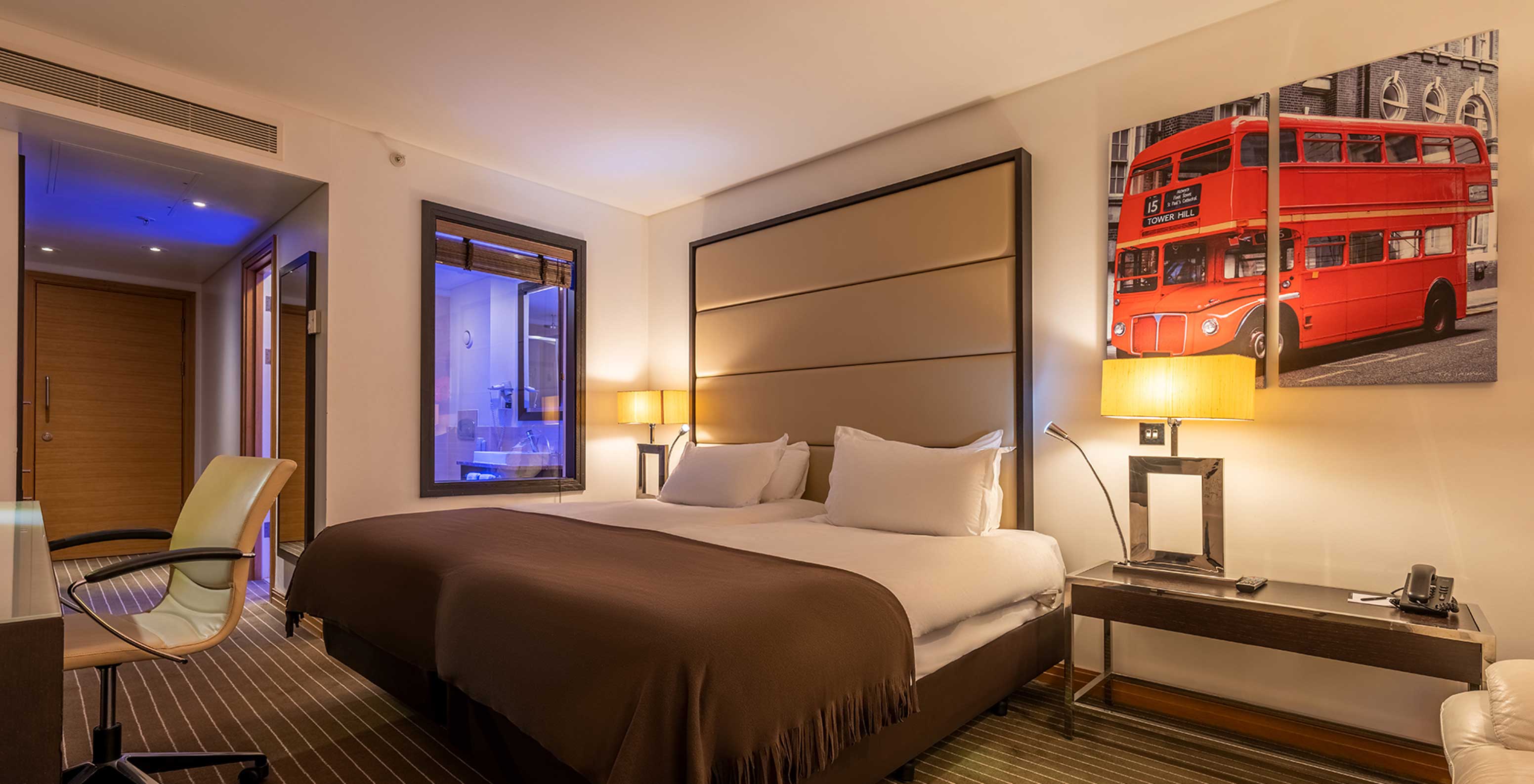 O Premium Twin do Pestana Chelsea Bridge tem duas camas com quadros de Londres na parede, mesa de cabeceira, sofá e cadeira