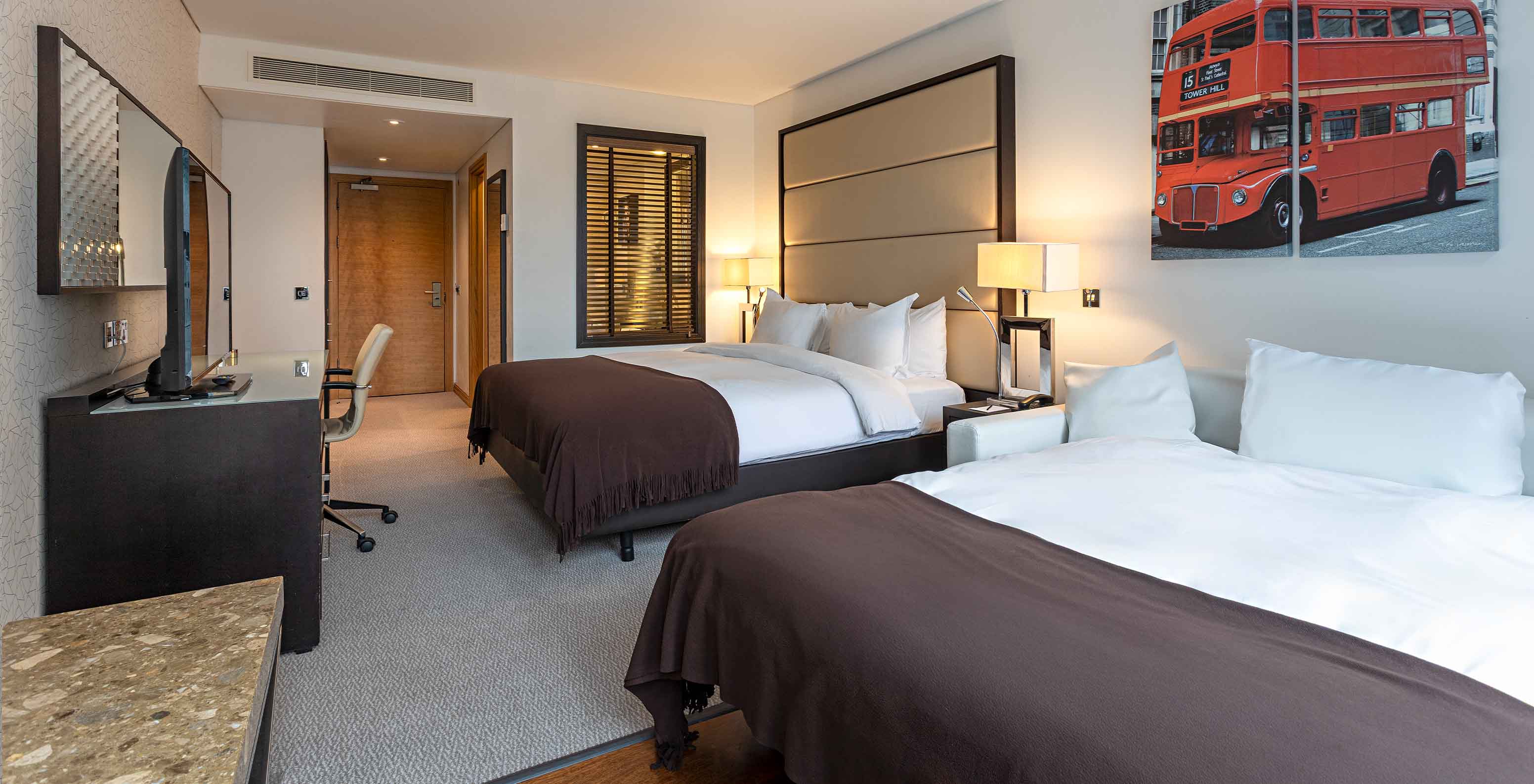 Quarto Deluxe Family Beds no Pestana Chelsea Bridge com duas camas, secretária e iluminação suave moderna