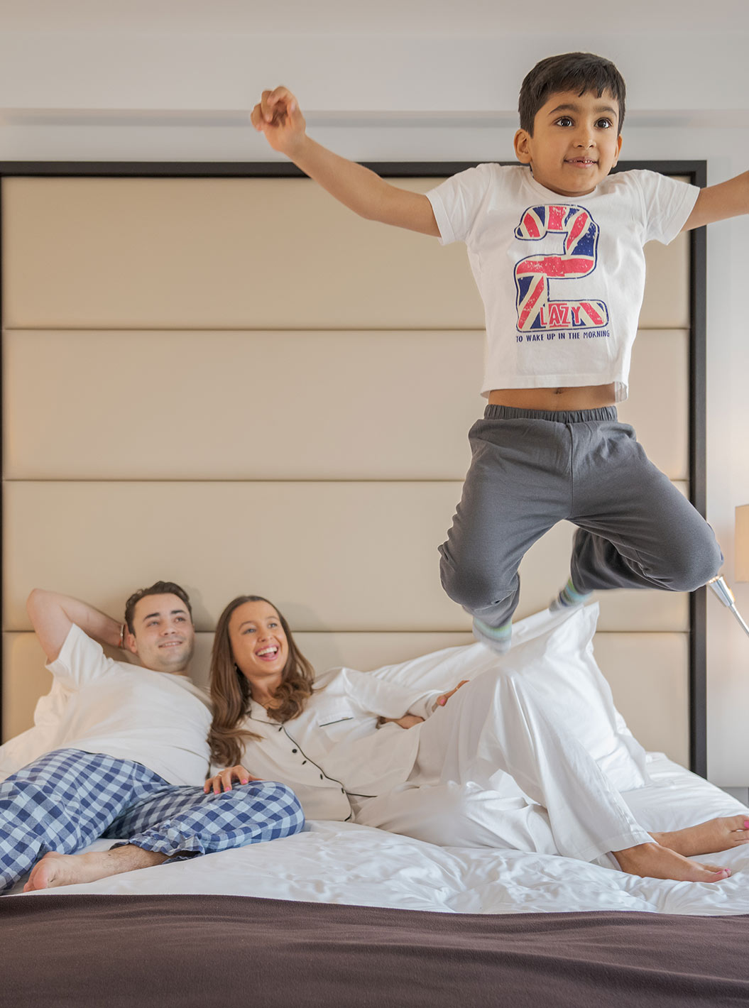 O Deluxe Family do Pestana Chelsea Bridge tem cama de casal com uma família deitada e uma criança a saltar