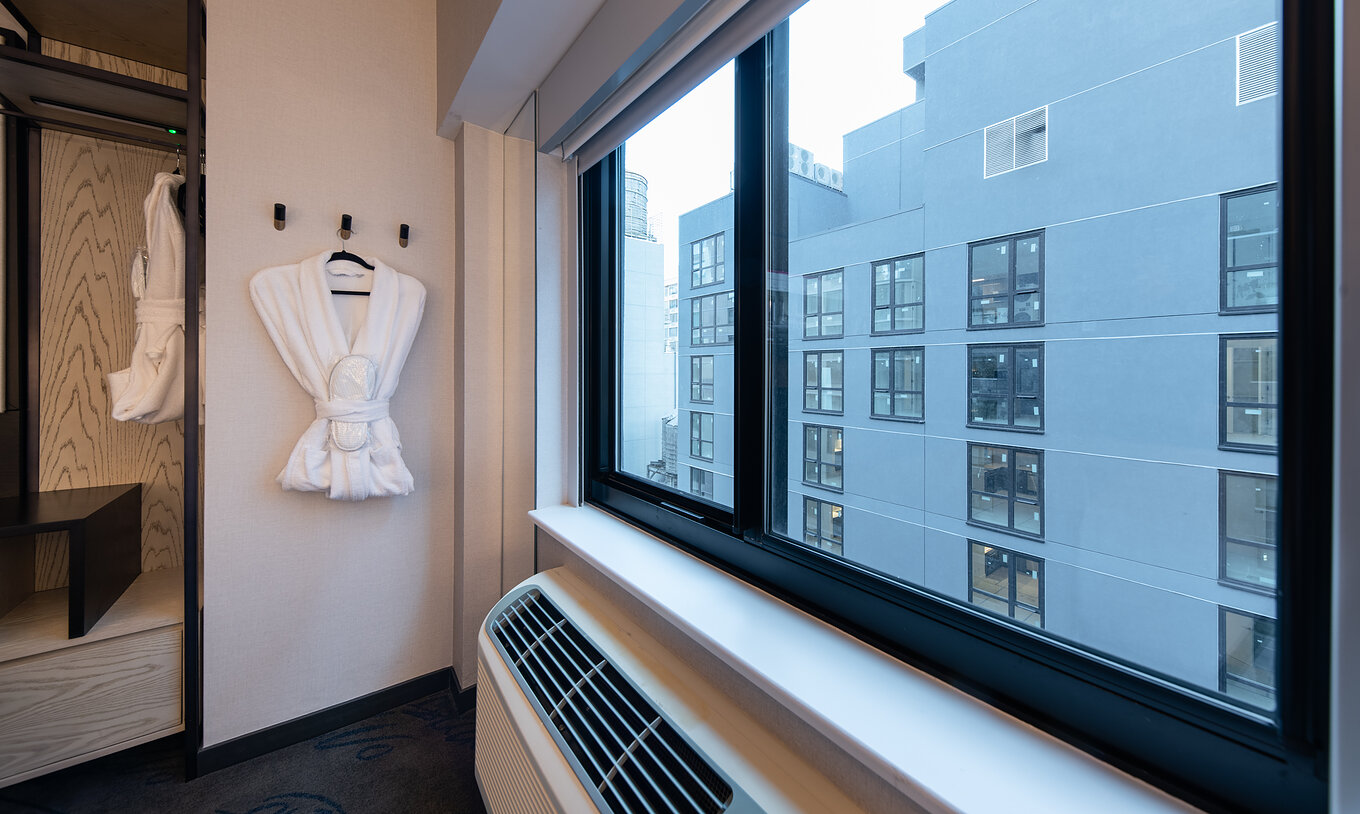 O Superior King High Floor ADA do Pestana CR7 Times Square tem um roupão e uma janela com vista para outro edifício