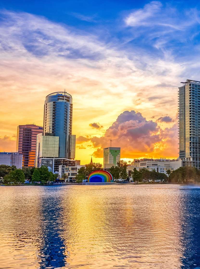 Paisagem urbana de Orlando ao pôr do sol, com um lago e um chafariz em primeiro plano