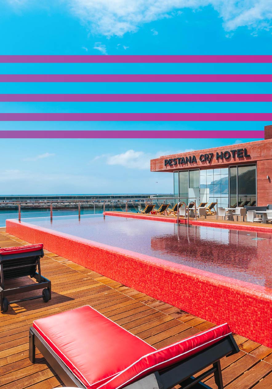 Piscina exterior vermelha junto ao Pestana CR7 Hotel com espreguiçadeiras e vista mar sob céu azul claro