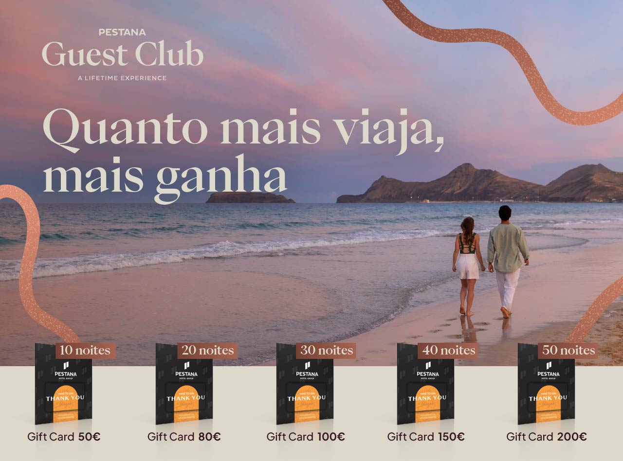 Casal caminha na praia ao entardecer com montanhas ao fundo e promoção Pestana Guest Club com cartões