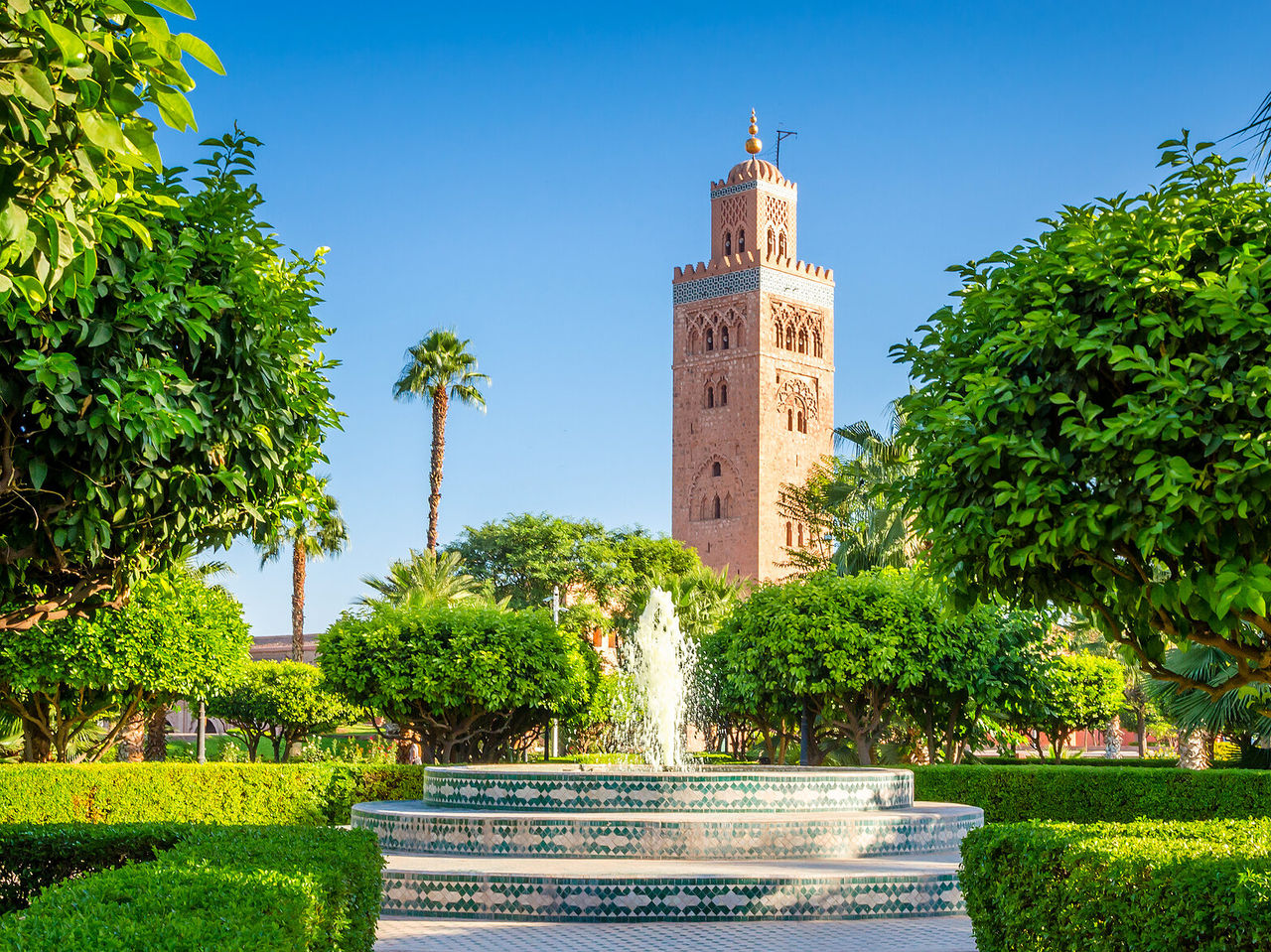 Blick auf die Koutoubia-Moschee, historisches Wahrzeichen, umgeben von Bäumen und einem typischen marokkanischen Brunnen