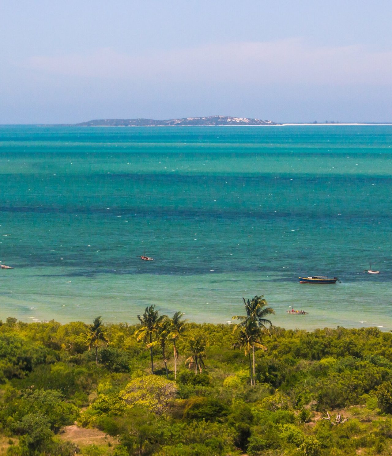 Luftaufnahme eines tropischen Strandes mit Palmen, Fischerbooten und kristallklarem Meer mit einer Insel im Hintergrund