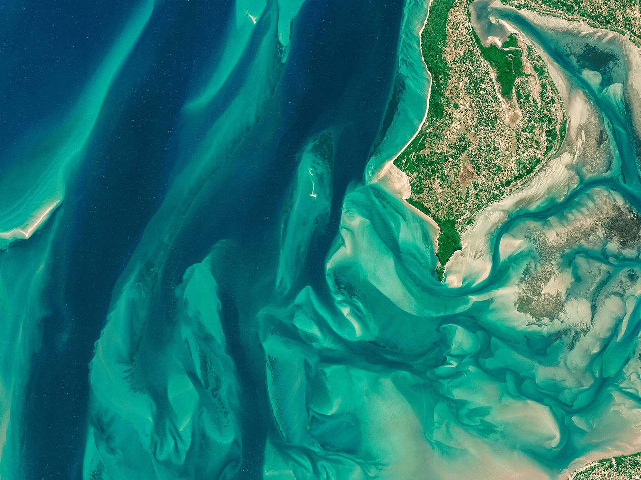 Luftaufnahme über grünen Ebenen und dem Ozean, die ein asymmetrisches Muster aus Sand und Wasser bilden