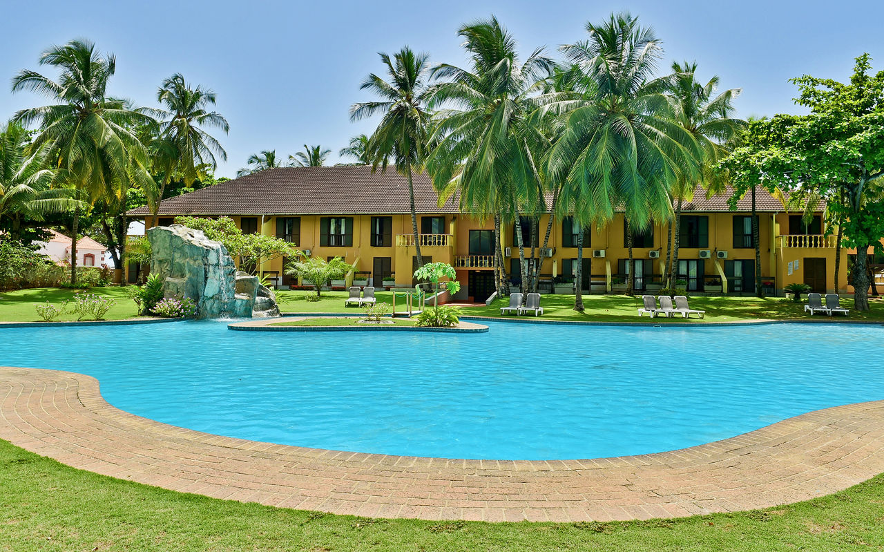 Gelbes Gebäude mit vielen Fenstern, Außenpool, Palmen und Liegen eines 4-Sterne-Hotels in São Tomé