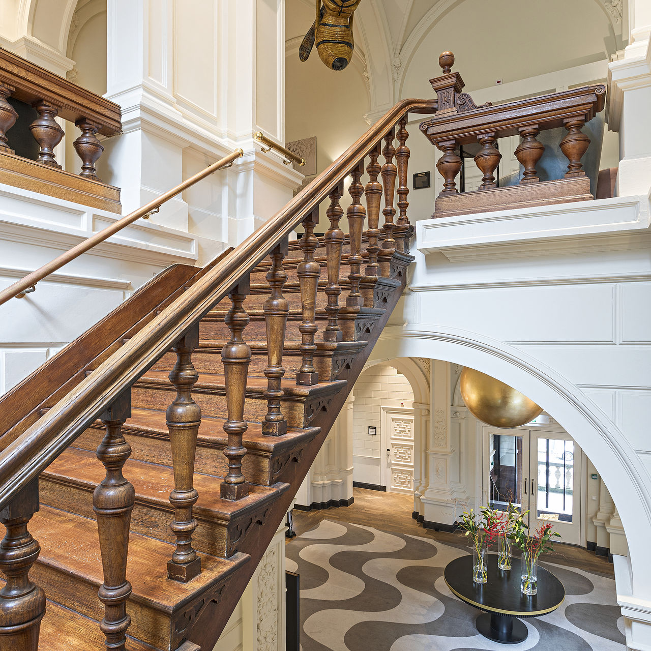 Escadas de madeira no interior do Pestana Amsterdam Riverside, com corrimão ornamentado, paredes brancas e vista para o hall