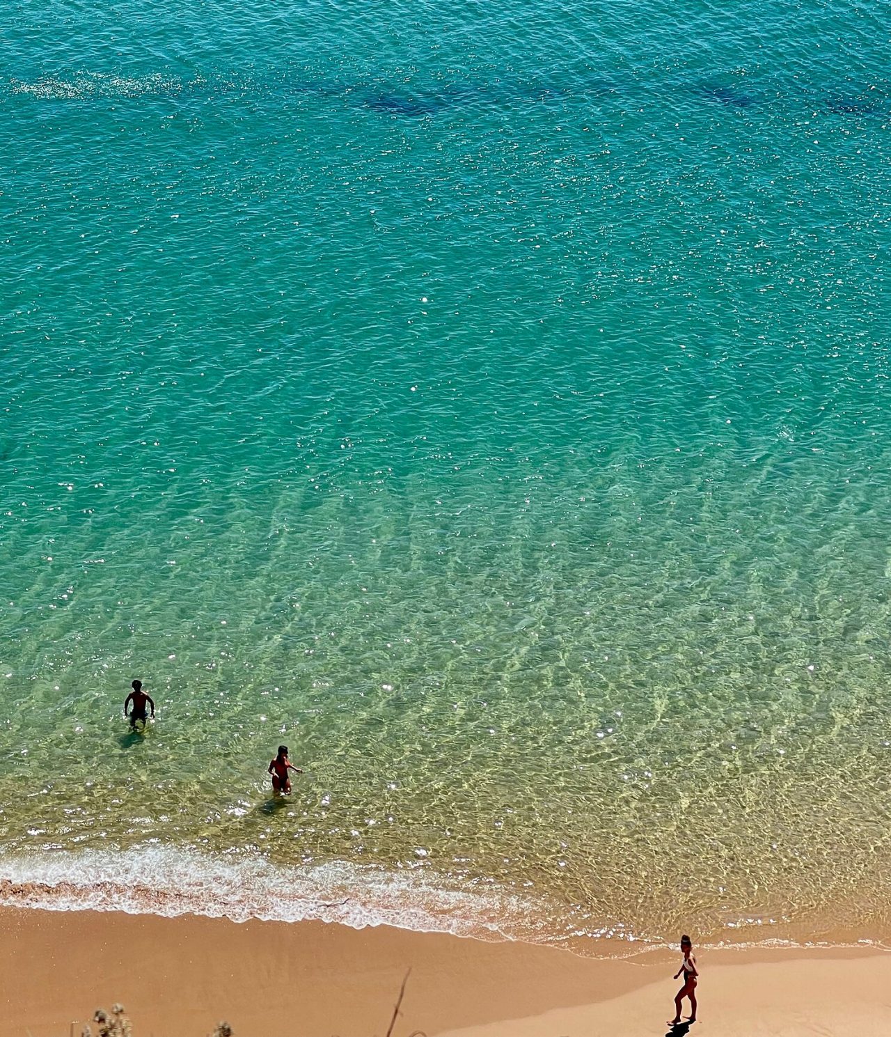 Luftaufnahme von zwei Personen, die an einem Strand mit klarem Wasser und goldenem Sand in der Algarve-Region schwimmen