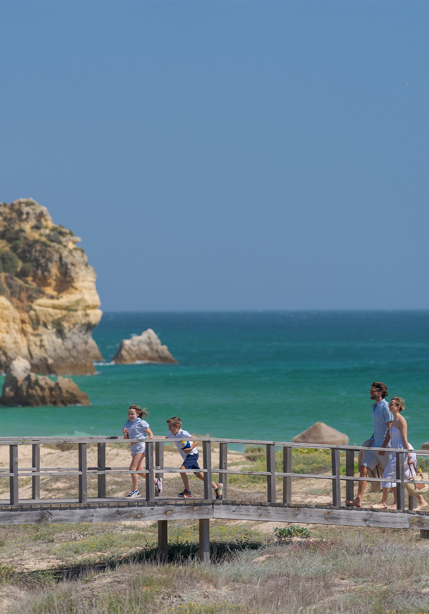 Holzstege der Strände von Alvor mit dem Meer im Hintergrund und zwei Kindern, die mit Eltern laufen