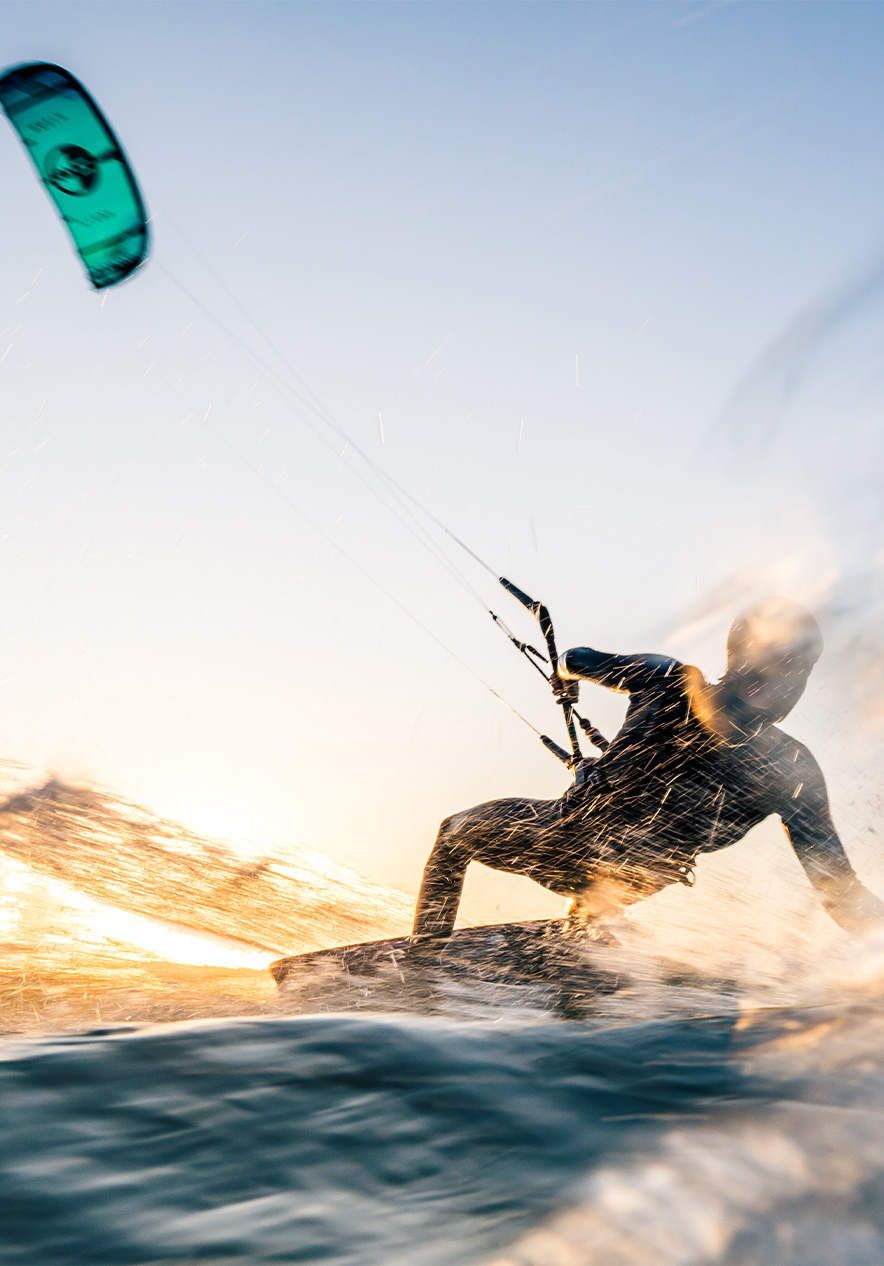 Mann macht Kitesurfen auf dem Meer mit blauer Segel, Wasser spritzt und die Sonne spiegelt sich im Wasser