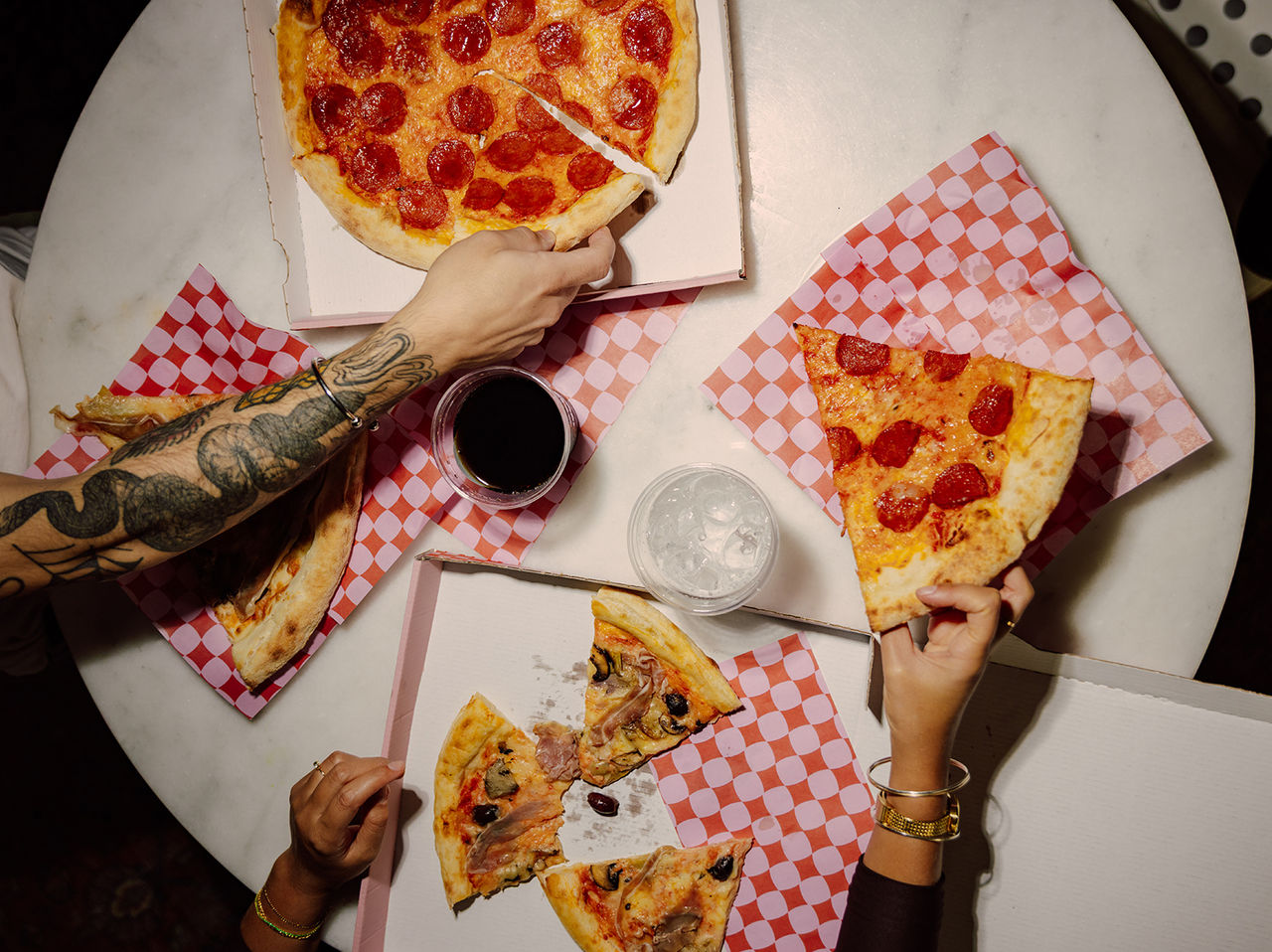 Pizzas servidas no restaurante do Pestana CR7 Funchal, sobre mesa redonda com mãos segurando fatias