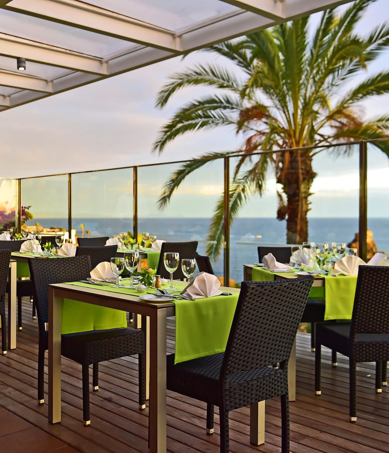 Das Restaurant The Deck im 4-Sterne-Hotel am Meer in Funchal hat mehrere Tische mit grünen Tischdecken und Meerblick