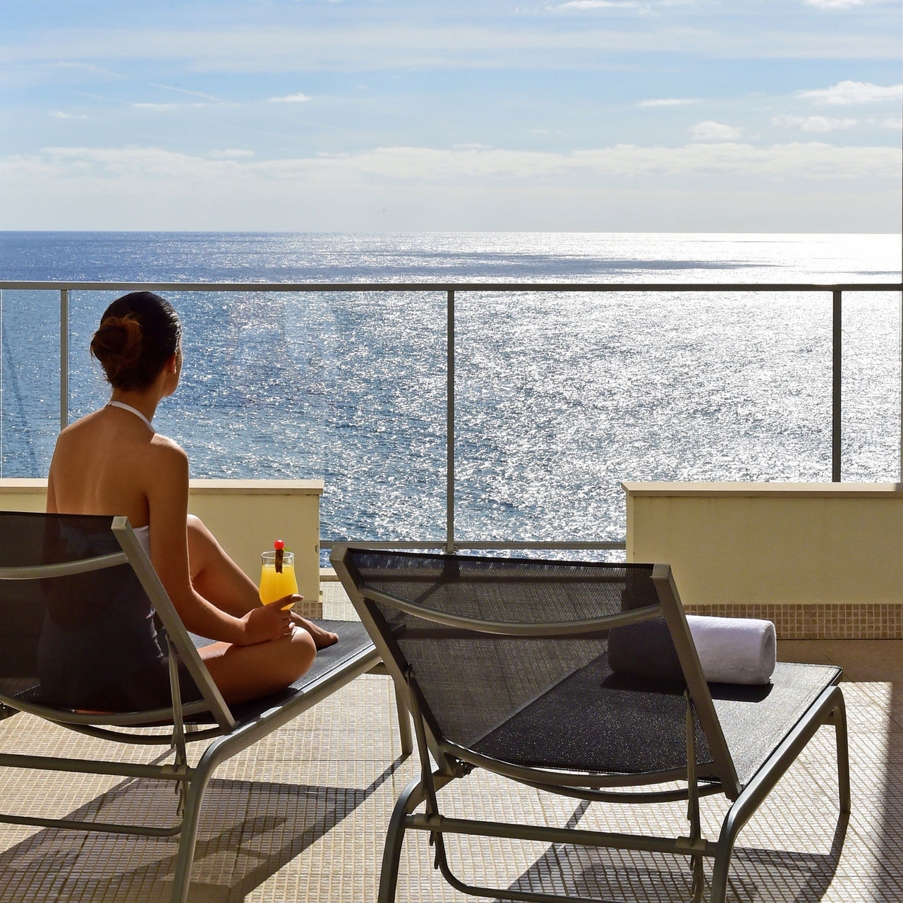 Frau sitzt auf einer Liege und trinkt einen Cocktail auf dem Balkon eines 4-Sterne-Hotels am Meer in Funchal