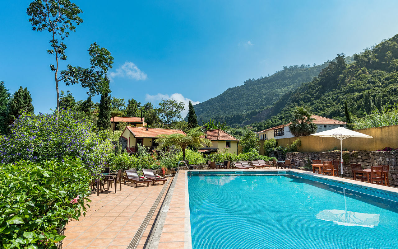 Pool des Pestana Quinta do Arco, ein Landhotel auf Madeira mit Liegen, Vegetation, Villen und Bergen
