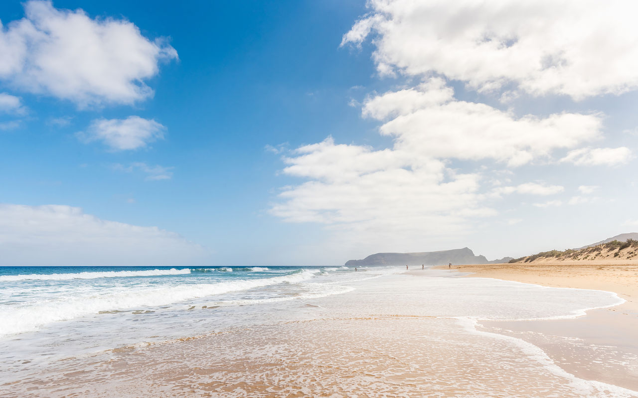 Langer Strand in Porto Santo mit hellem Sand, ruhigen Wellen und blauem Himmel mit einigen Wolken
