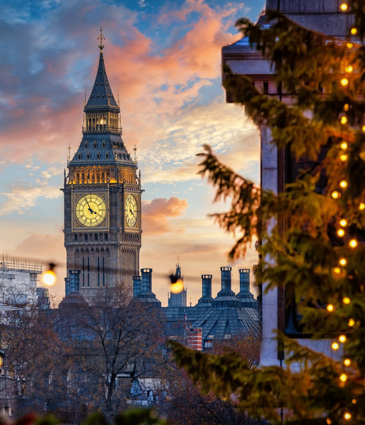 Blick von hinter einem Baum auf den berühmten Big Ben, mit seiner Uhr mit goldenen Details und schwarzen Zeigern