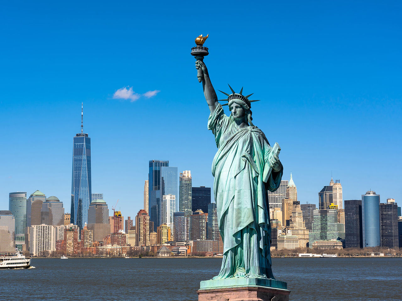 Stadtlandschaft von New York mit der Freiheitsstatue im Vordergrund und der Skyline von New York im Hintergrund