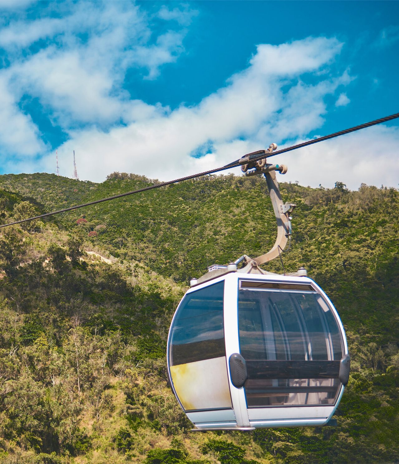 Seilbahnkabine bewegt sich über einen Berg in Caracas, umgeben von Vegetation und blauem Himmel im Hintergrund