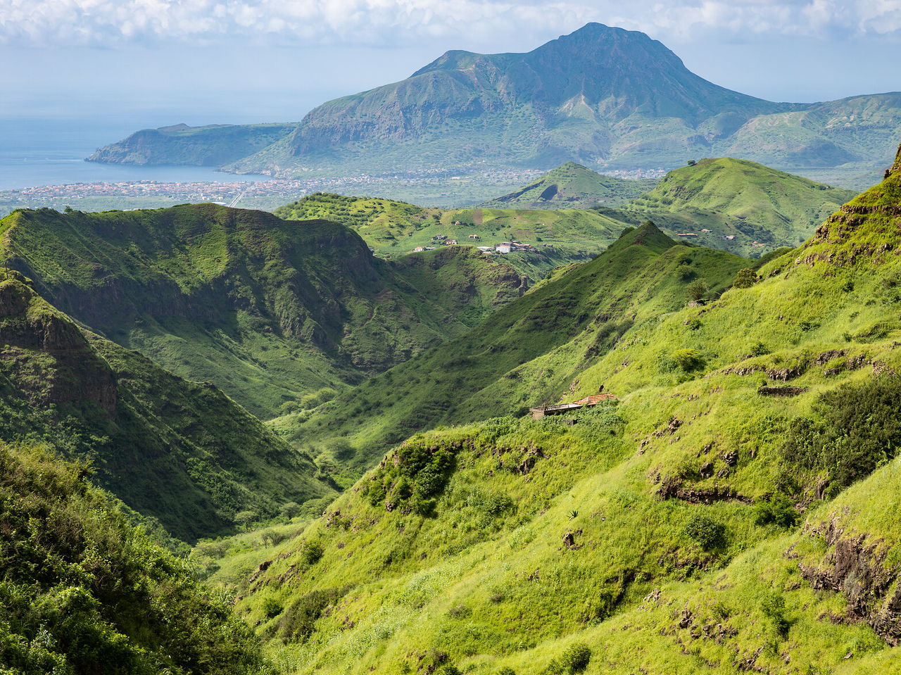Landscape with lush green mountains stretching to the horizon, with the city and blue sea in the distance
