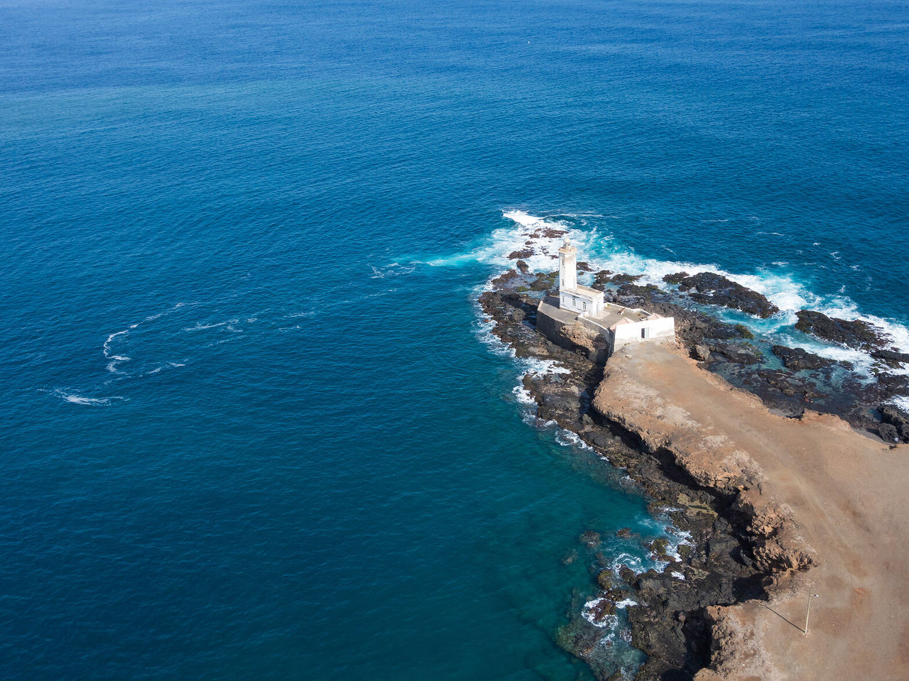 Explore Hotels in Cidade da Praia with an aerial view of a lighthouse on rocky cliffs above blue Atlantic waters