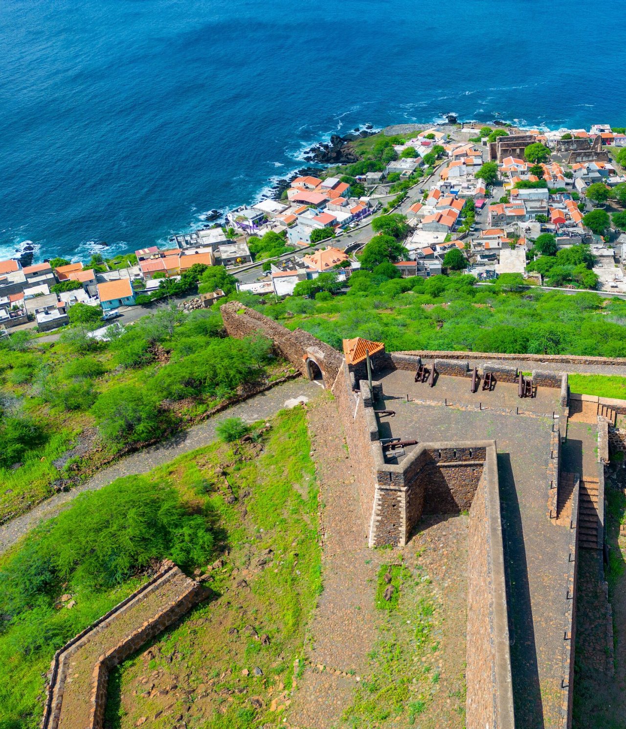 Explore Hotels in Cidade da Praia featuring an aerial view of coastal rooftops beside a historic stone fortress