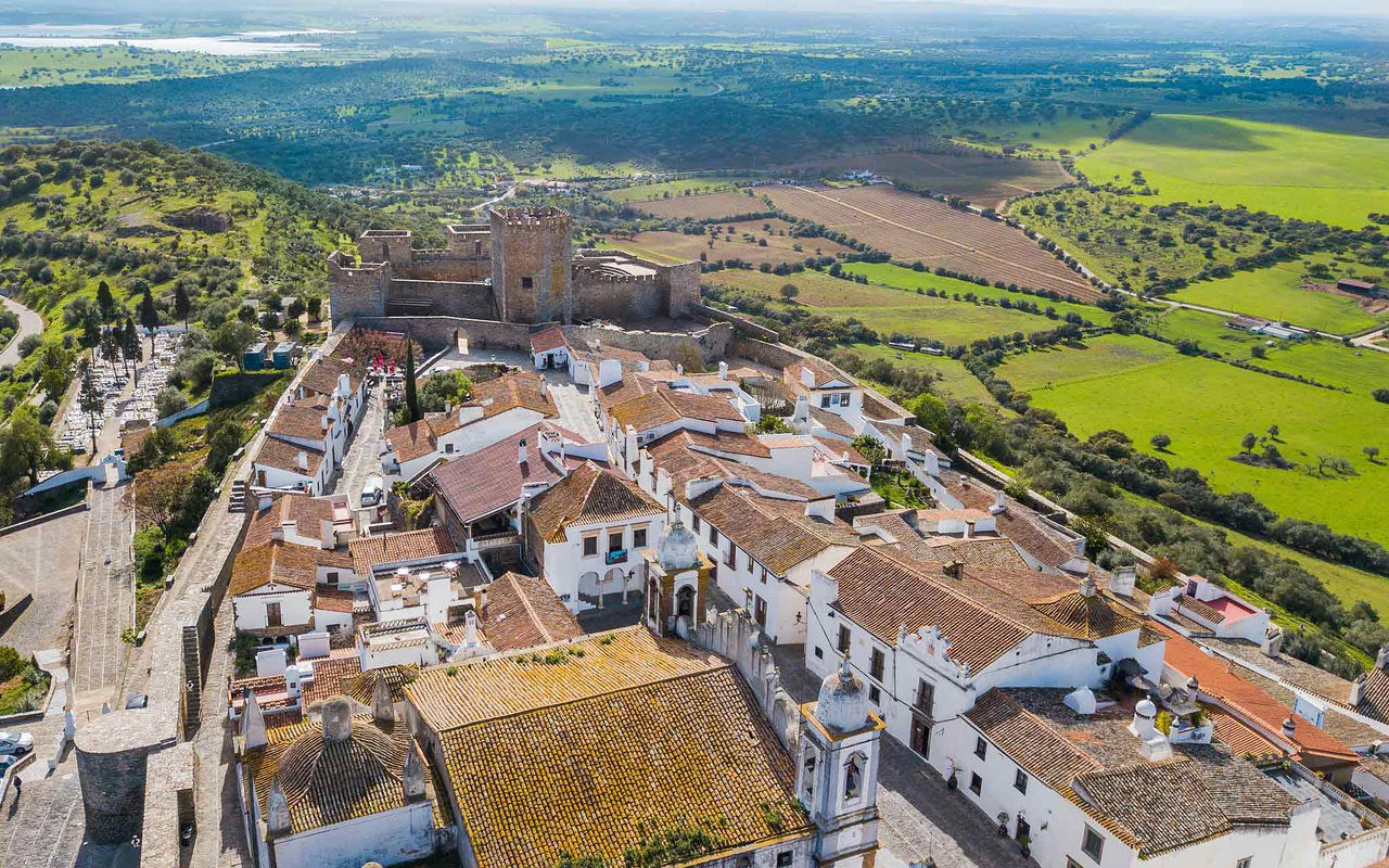 Explore Hotels in Alentejo with an aerial view of a hilltop village, stone castle and green farmland
