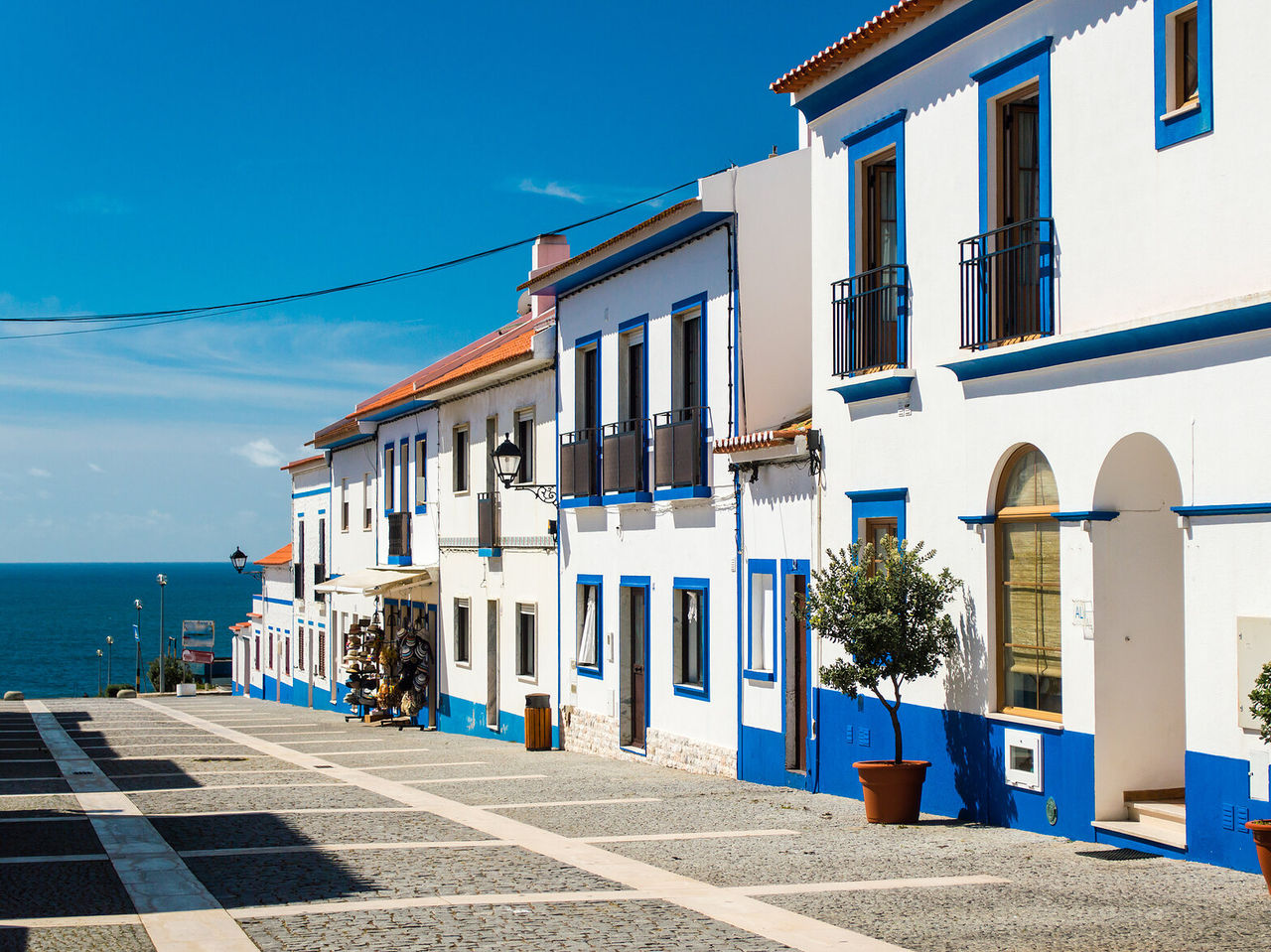 Explore Hotels in Alentejo featuring white coastal houses with blue trim along a cobblestone street by the sea