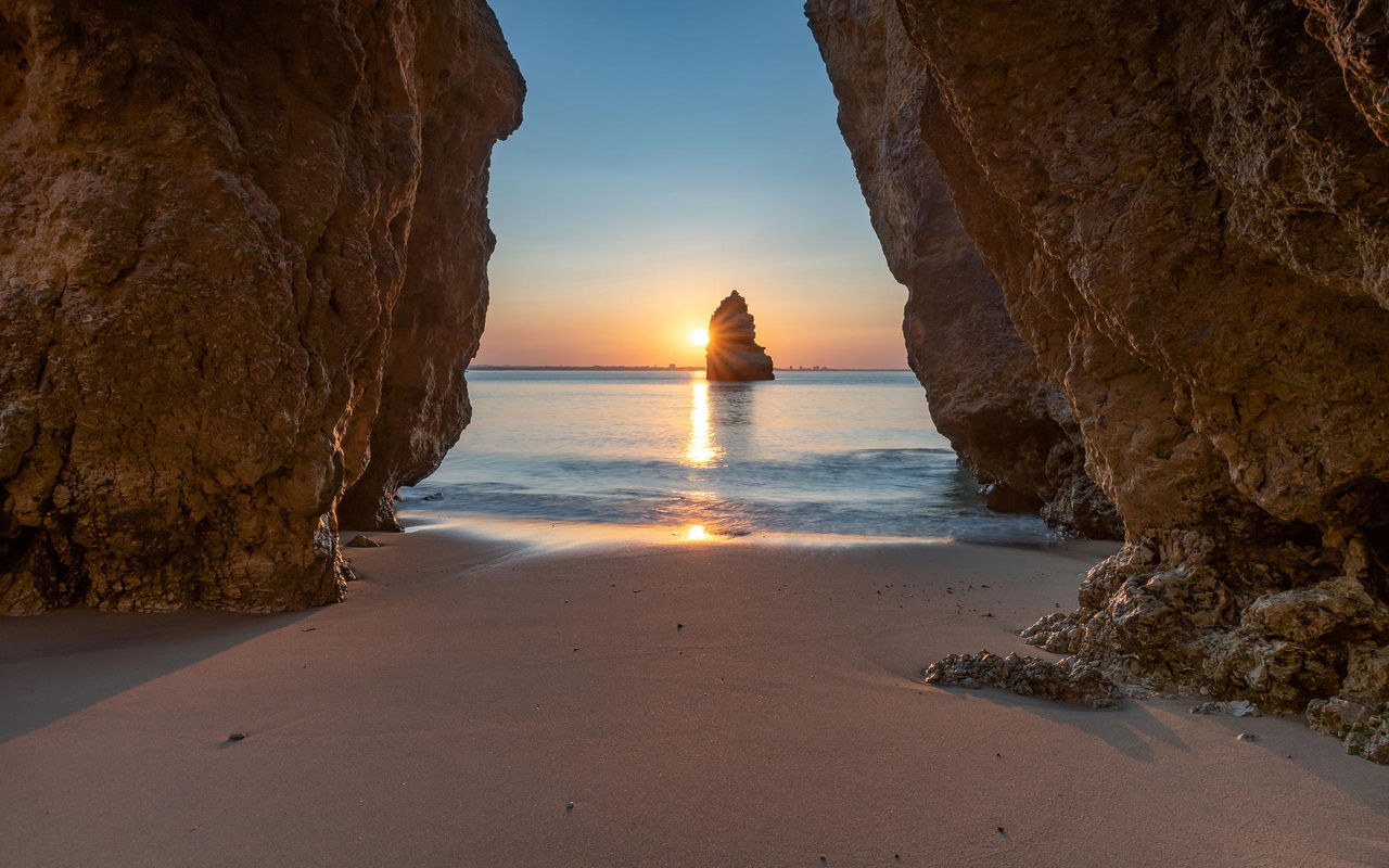 Discover our best tips for your next trip to Algarve on Pestana Stories, featuring a sunset beach framed by cliffs