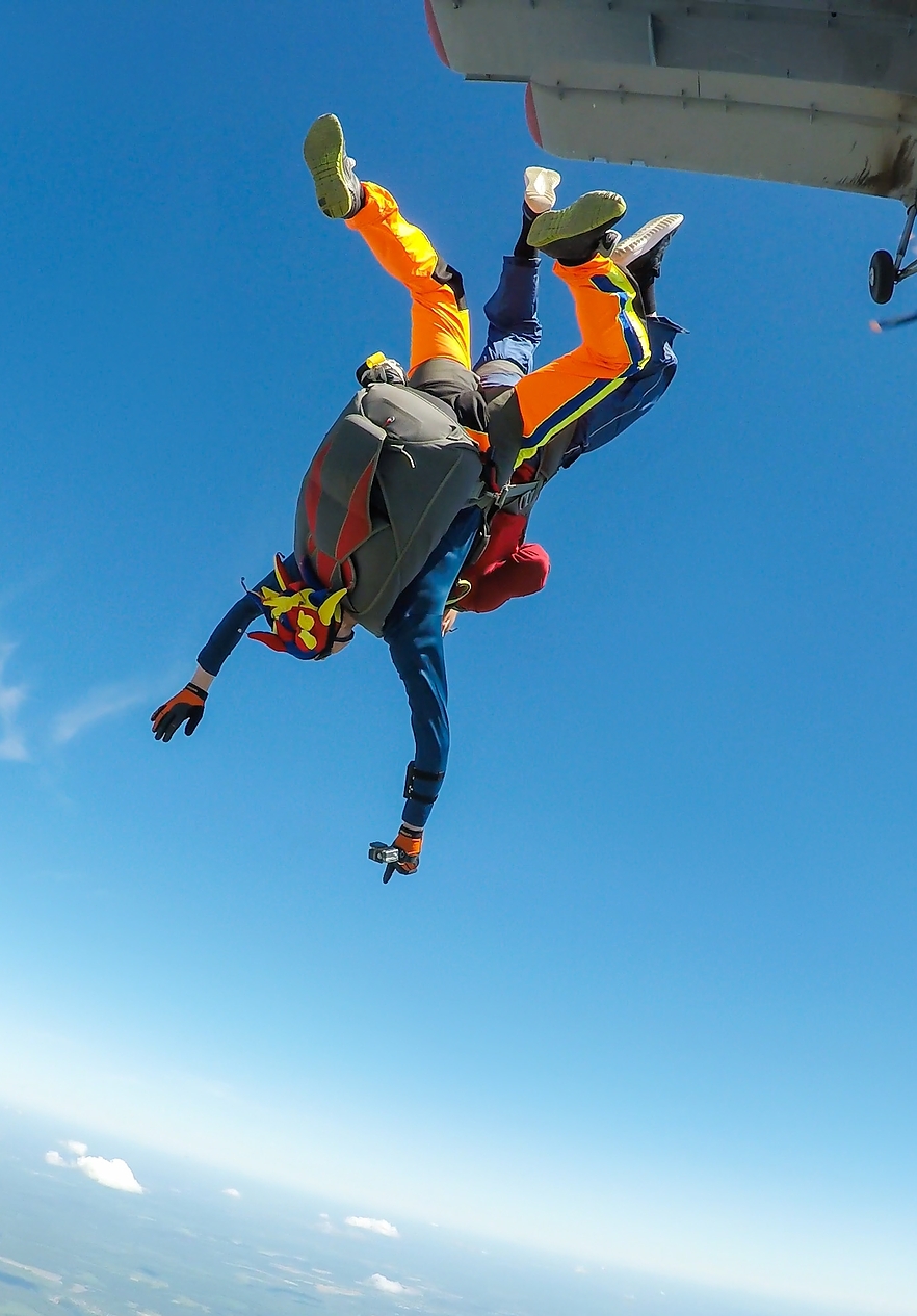 Person in free fall after jumping from a plane wearing a parachuting jumpsuit and helmet accompanied by an instructor