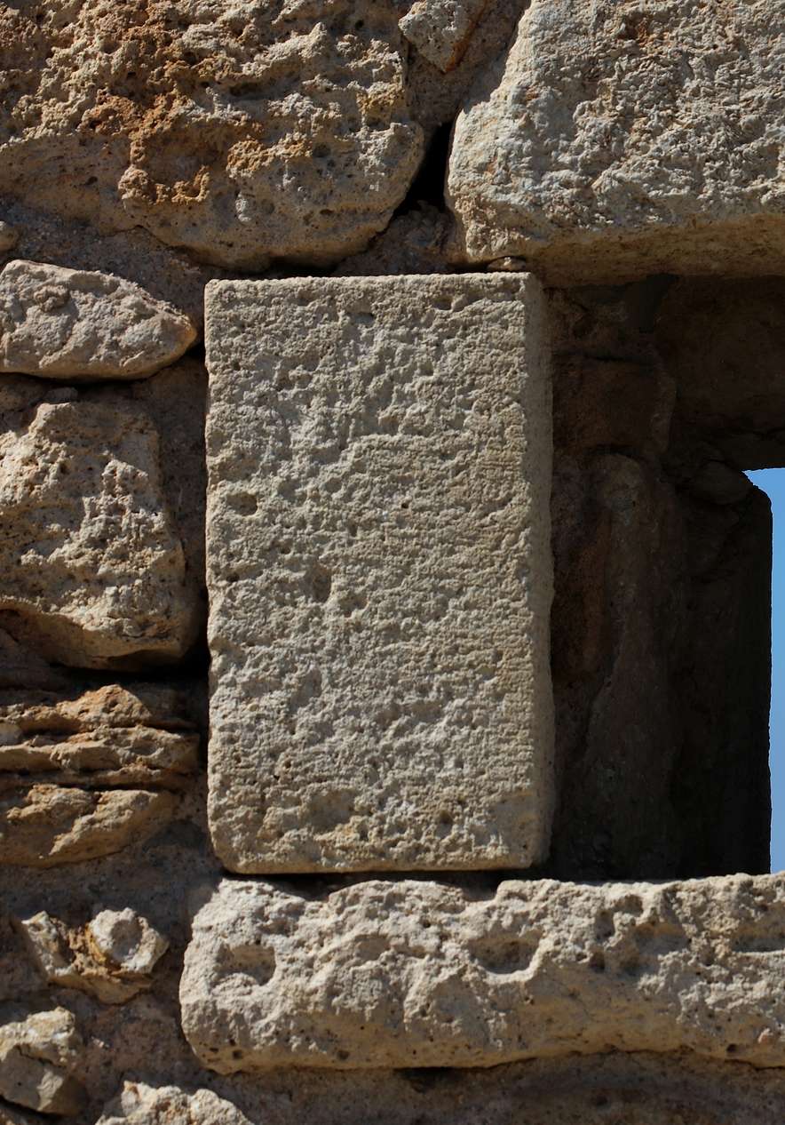 Narrow window in a wall of rustic stones in Armação de Pêra with a view of the blue sky in the background