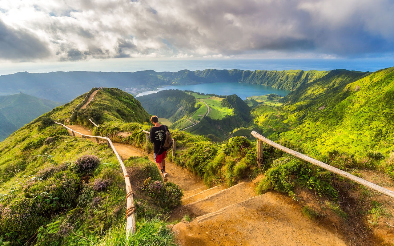 Explore Hotels in the Azores overlooking a hiker on mountain trails above a crater lake and green hills