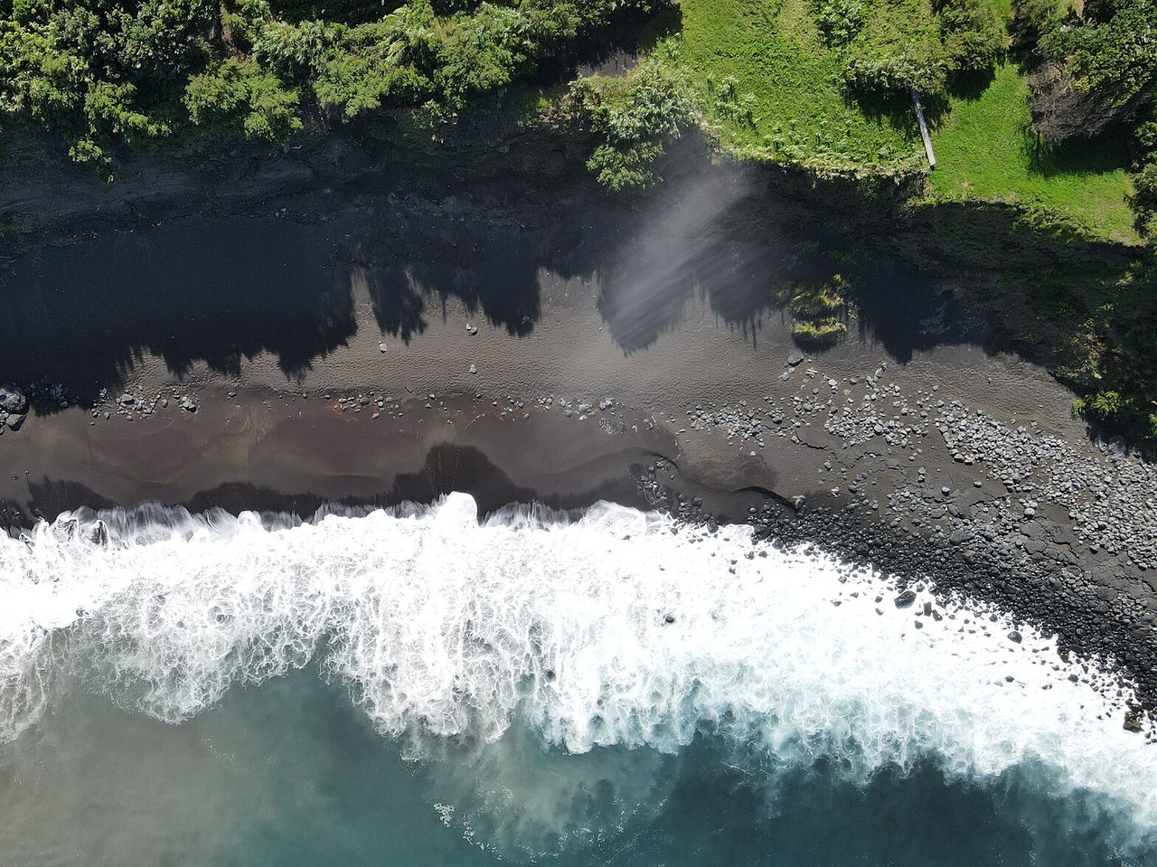 Explore Hotels in the Azores with an aerial view of dark volcanic sand, foamy waves and lush coastline