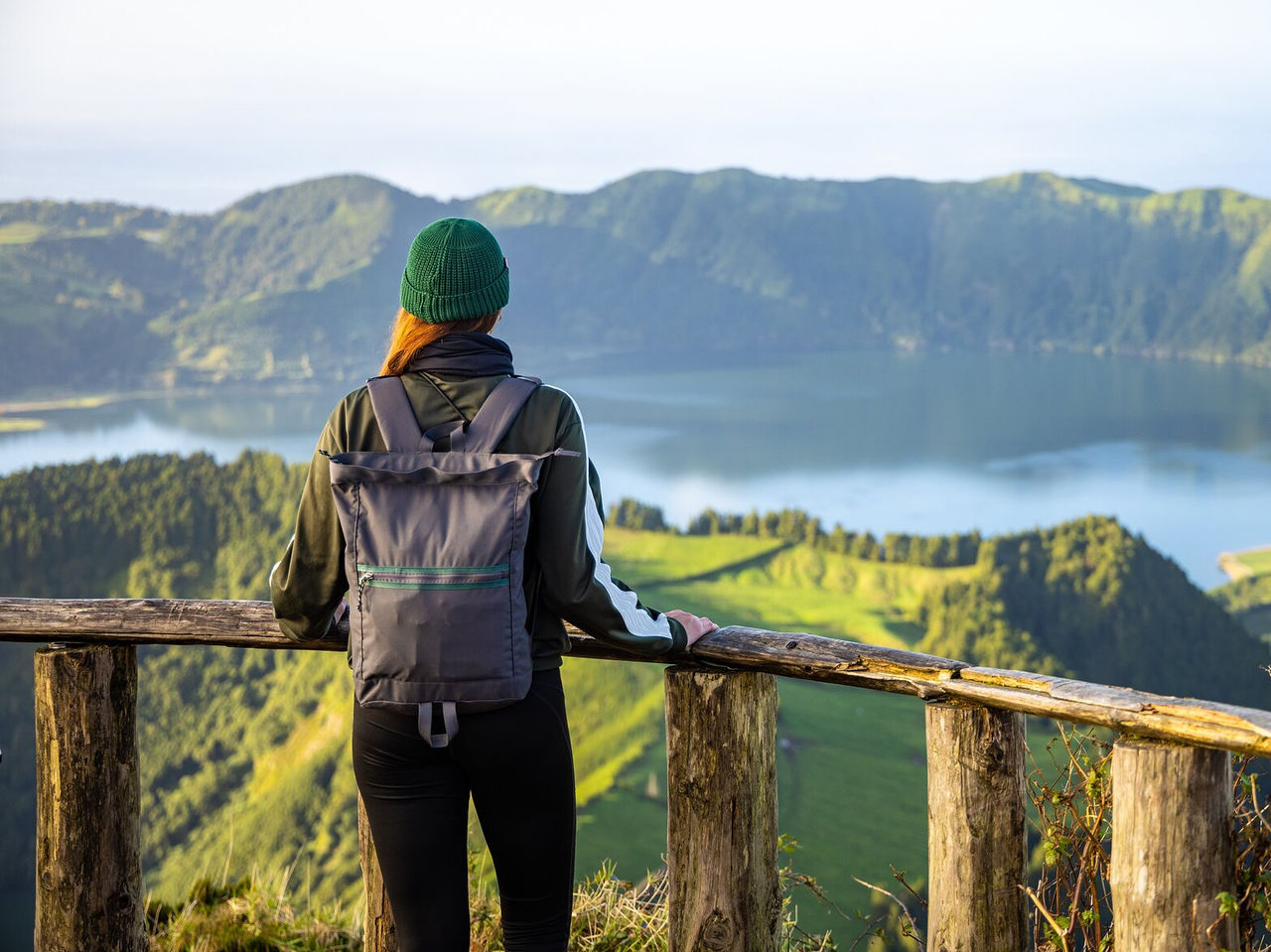Explore Hotels in the Azores featuring a traveler overlooking a volcanic lake and green mountain cliffs